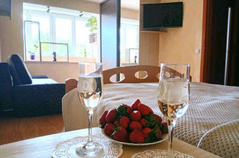 Уютная спальня с кроватью, столиком у окна, двумя бокалами и тарелкой свежей клубники.