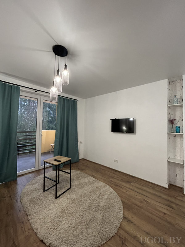 Светлая гостиная с круглым ковром, черным столиком, подвесными светильниками и выходом на балкон с жёлтой стеной.