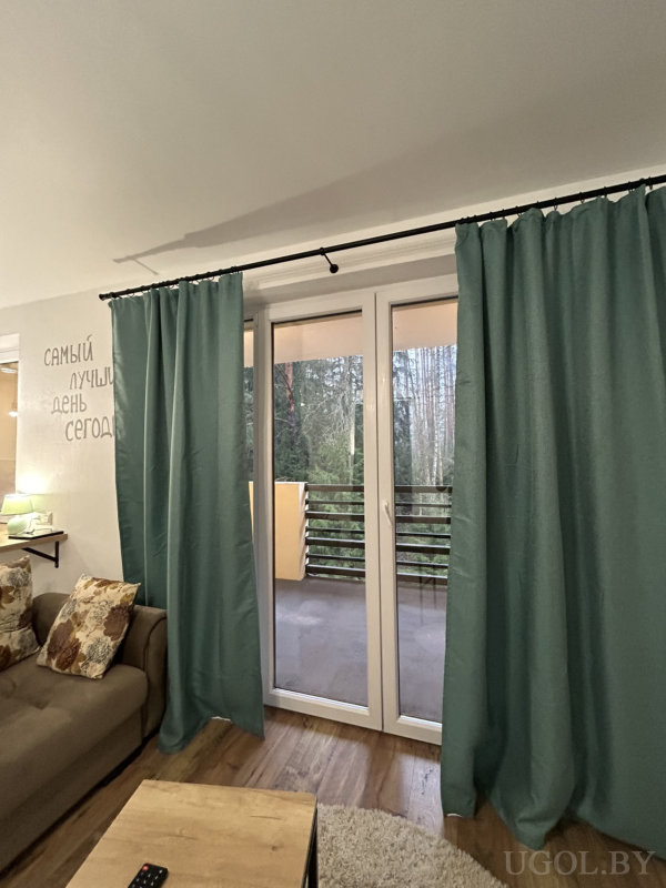 Тёплая гостиная с коричневым диваном, деревянным столиком, балконом с видом на лес и мотивационной надписью на стене.