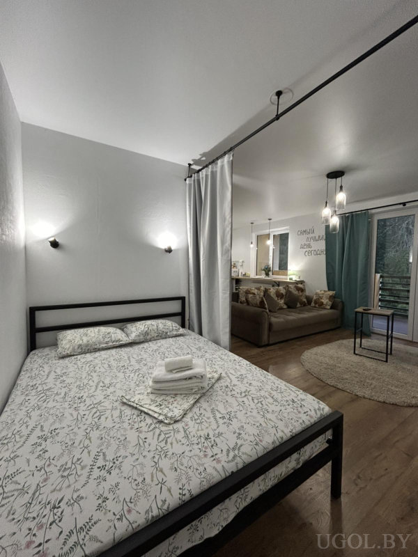 Кровать с цветочным текстилем, коричневый диван, круглый ковёр, балкон с бирюзовыми шторами и надписью «САМЫЙ ЛУЧШИЙ ДЕНЬ СЕГОДНЯ».