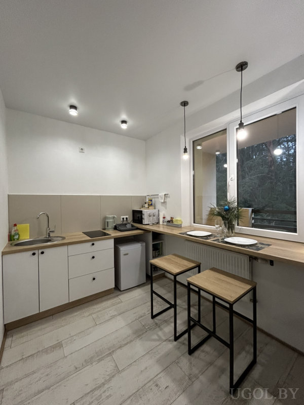 Компактная кухня с белыми шкафами, деревянной барной стойкой, двумя табуретами и сервировкой на двоих.