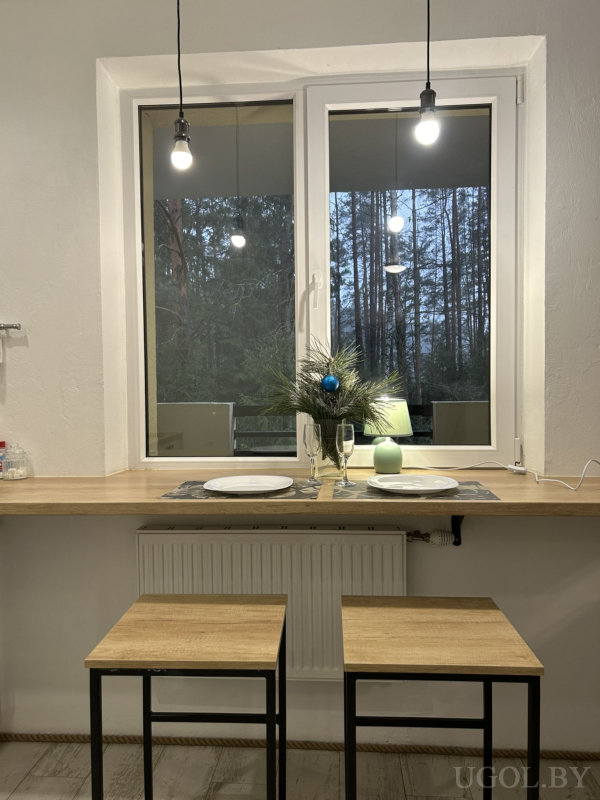 Деревянная стойка у окна с сервировкой на двоих, подвесными светильниками и декоративной композицией из еловых веток.