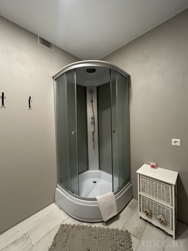 Угловая душевая кабина, белый шкаф с плетёными ящиками, красная свеча и светло-серые стены.