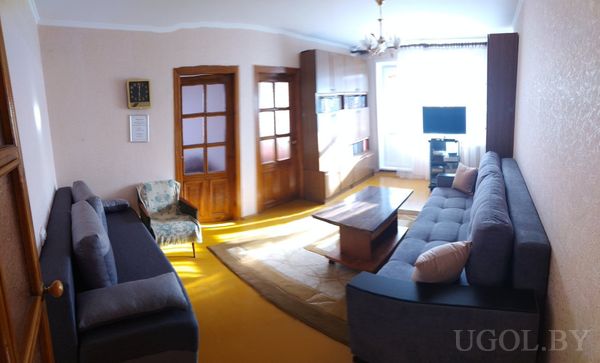 Уютная гостиная с двумя серыми диванами, деревянным столиком на ковре, телевизором у окна и встроенными шкафами.