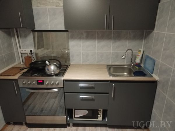 Современная кухня с плитой, мойкой, тёмными шкафами, встроенной микроволновкой и серым фартуком из плитки.