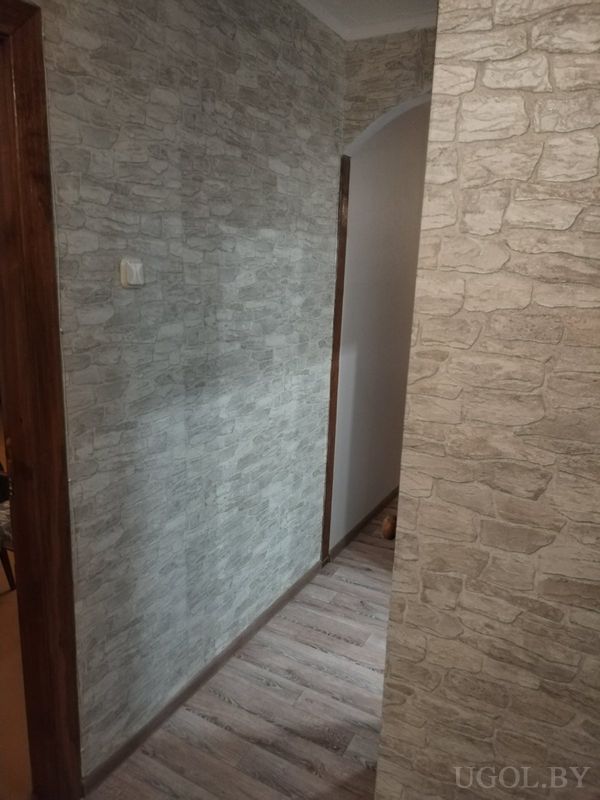 Уютный коридор с деревянным полом, арочным проёмом и стенами с обоями под каменную кладку.