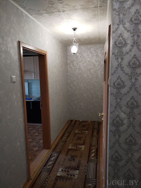 Узкий коридор с ковровой дорожкой, серыми стенами, арочным проёмом и дверями по бокам.