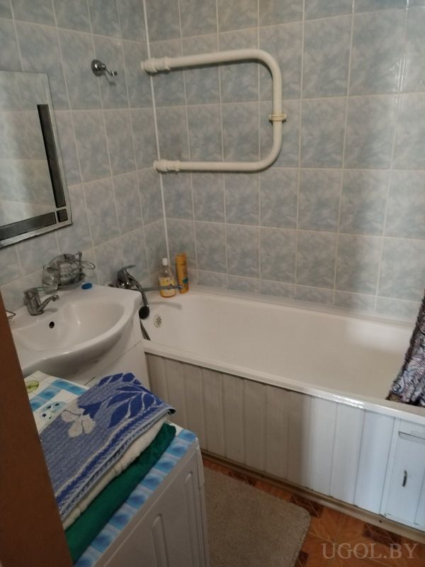 Компактная ванная с белой ванной, умывальником с зеркалом и стиральной машиной с полотенцами.