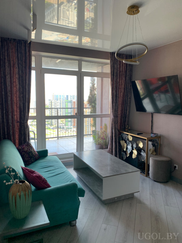 Современный интерьер с бирюзовым диваном, глянцевым потолком и выходом на балкон с панорамой высоток.