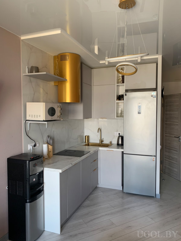 Современная кухня с серыми фасадами, белой столешницей, встроенной техникой и золотой вытяжкой.