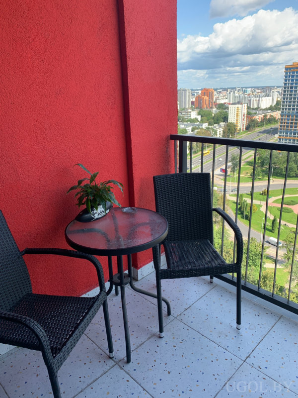 Уютное место с плетёной мебелью, растением и видом на высотки и зелёные зоны.