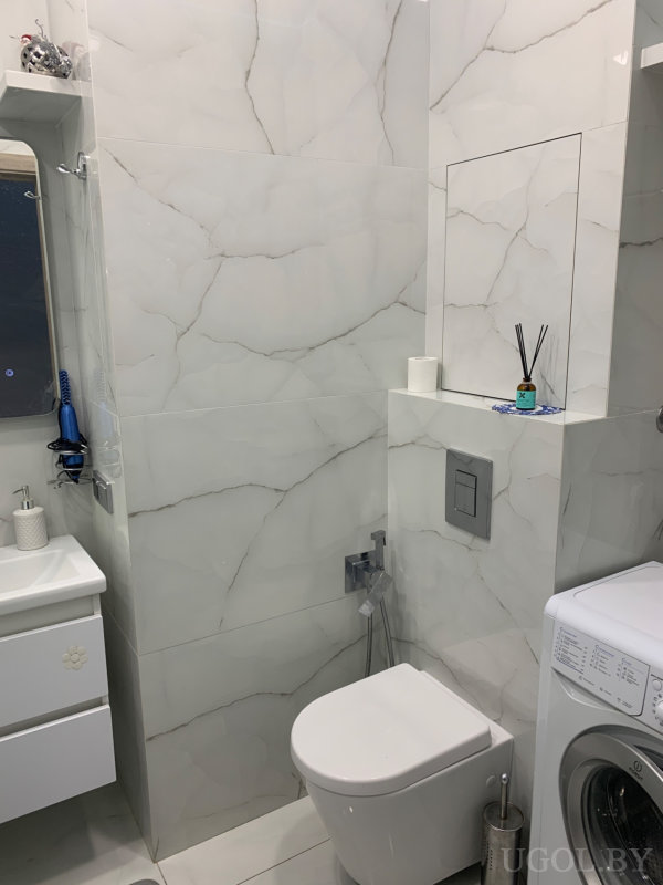 Чистый и функциональный дизайн с мраморной плиткой, подвесным унитазом и зеркалом над раковиной.