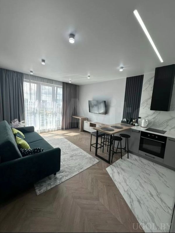 Открытая студия с диваном, телевизором, барной стойкой и кухней с мраморным фартуком и встроенной техникой.