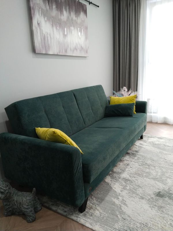 Комната с диваном, жёлтыми подушками, картиной на серой стене и декоративной композицией у окна.