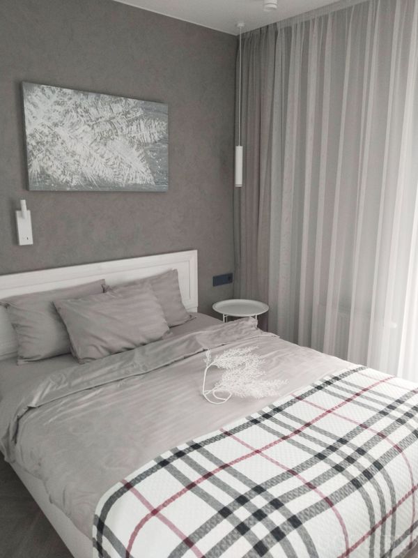 Минималистичная спальня с серыми стенами, белым изголовьем, клетчатым пледом и двумя подвесными лампами.