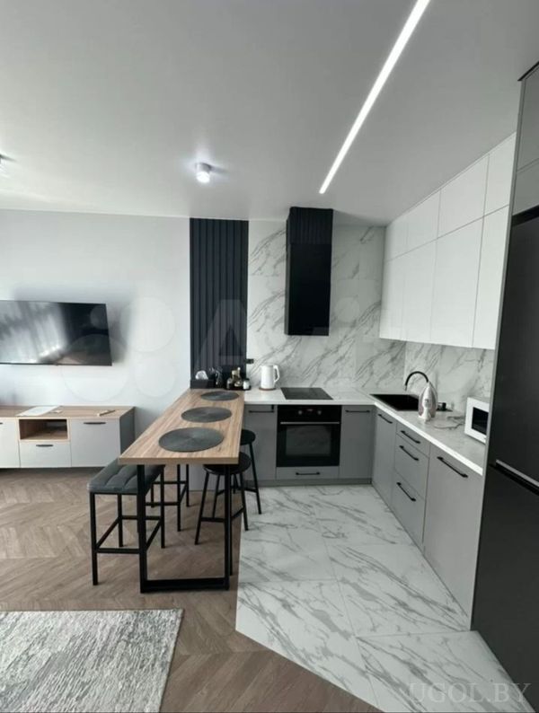 Кухонная зона с белыми и серыми фасадами, барной стойкой, техникой и переходом в зону гостиной.