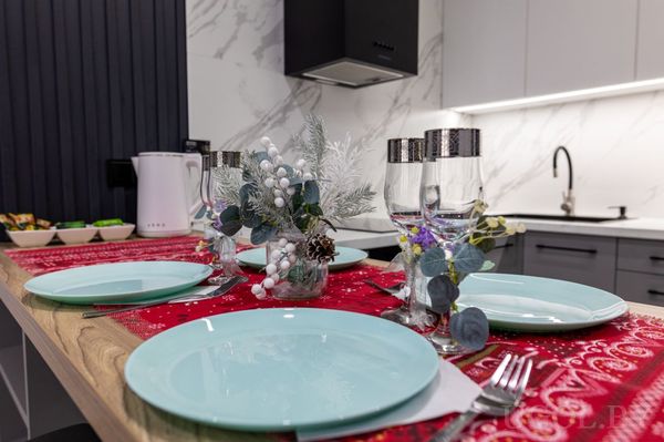 Праздничная сервировка на деревянной столешнице с голубыми тарелками, красными салфетками и зимним декором.