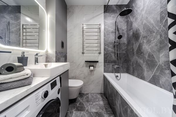 Современная ванная с умывальником, стиральной машиной, подвесным шкафом и душем с геометричной шторкой.