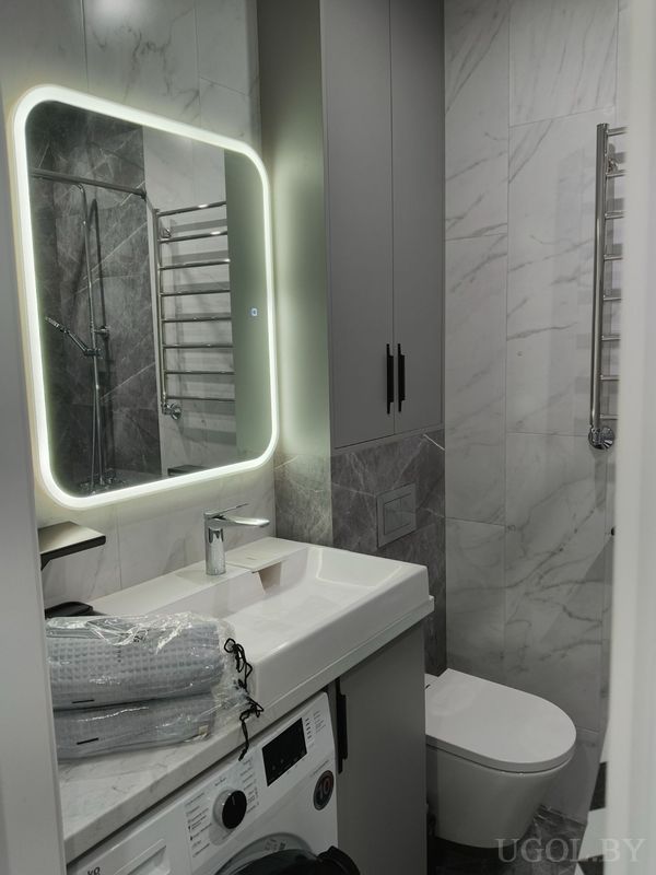 Интерьер с мраморной плиткой, умывальником, стиральной машиной, подвесным шкафом и душевой зоной.