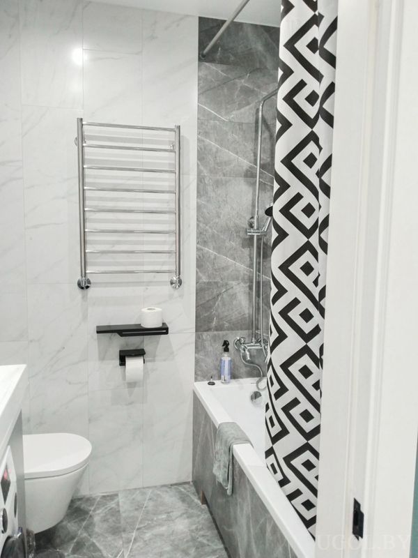 Комната с мраморной плиткой, унитазом, ванной с шторкой, стиральной машиной и настенным полотенцесушителем.