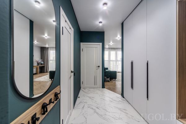 Светлый коридор с белыми дверями, зеркальным шкафом, круглым зеркалом и деревянной панелью с крючками.