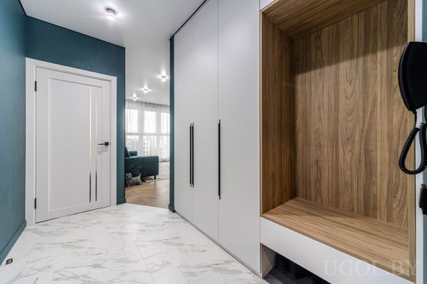 Интерьер с белыми фасадами, деревянной нишей с лавкой и выходом в гостиную с окнами.