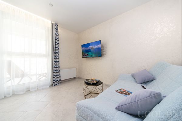 Светлая гостиная с голубым диваном, журнальным столиком, телевизором и шторами с зигзагами у окна.