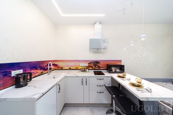 Современная кухня с белыми фасадами, фартуком с пейзажем, барной зоной и золотой сервировкой.