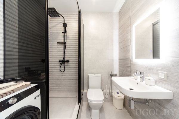 Компактная ванная с душевой кабиной, стиральной машиной, умывальником и зеркалом с подсветкой.