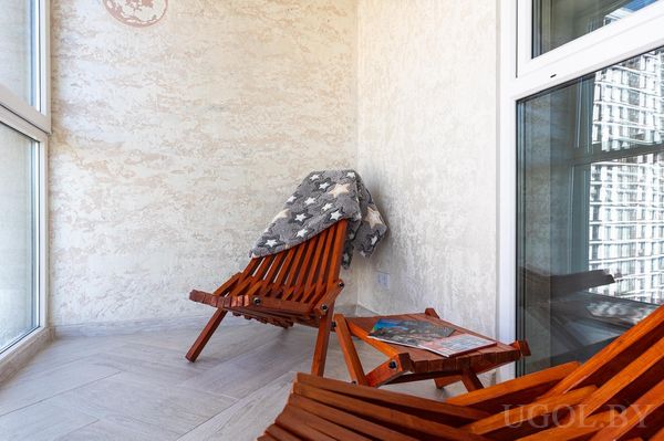 Уютный балкон с двумя креслами, пледом в звёздном узоре, столиком и видом на высотки.