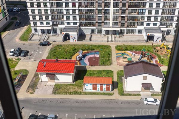 Панорама двора с двумя детскими площадками, дорожками, машинами и многоэтажкой на фоне.