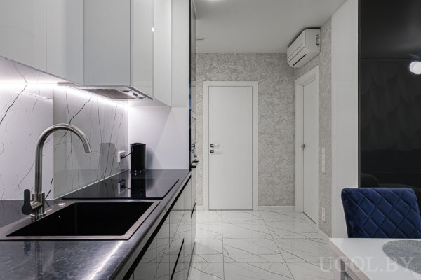 Кухня с белыми верхними и чёрными нижними шкафами, мраморным фартуком, чёрной мойкой и частью обеденной зоны с синей стуловой группой.