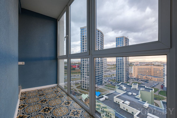 Застеклённая лоджия с панорамным видом на город, узорной плиткой на полу и синими стенами.