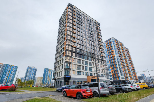 Современные высотные дома с разноцветными панелями, парковка с машинами, включая красный Mini Cooper, чистая городская среда.