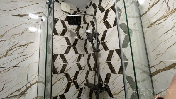 Стена с объёмным кубическим рисунком, мраморные боковые панели, верхний душ и ручная лейка за стеклянными перегородками.