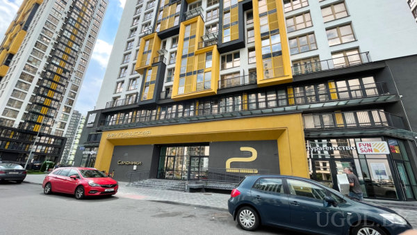 Фасад с бело-чёрно-жёлтыми панелями, большая жёлтая рама и номер «2», вывески «Європейка», «Європейська площа», «FUN SUN», «Управляюча компанія».