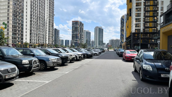 Современные жилые здания с балконами и большими окнами, припаркованные машины по обеим сторонам и плотная городская застройка.