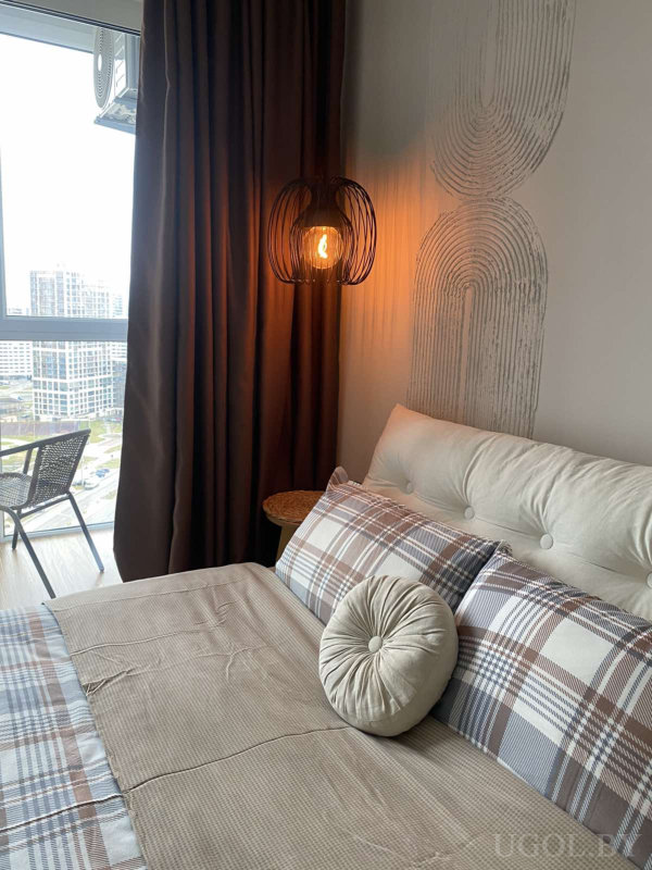 Кровать с подушками, настенное освещение, круглый столик, окно с балконом и панорамой высоток.