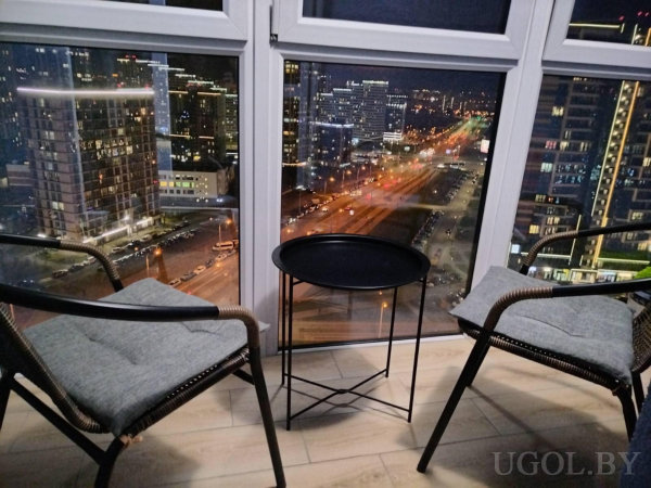 Два кресла и столик у окна, за стеклом — огни города, дороги и высотные здания.