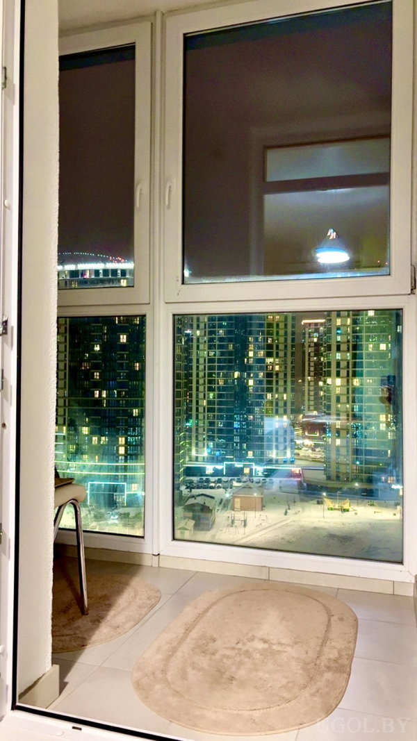 Ночная сцена с панорамным остеклением, светом, отражениями и зимним городским пейзажем.