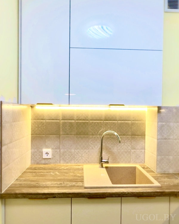 Рабочая зона с бежевой раковиной, розеткой, деревянной столешницей и светом под шкафами.