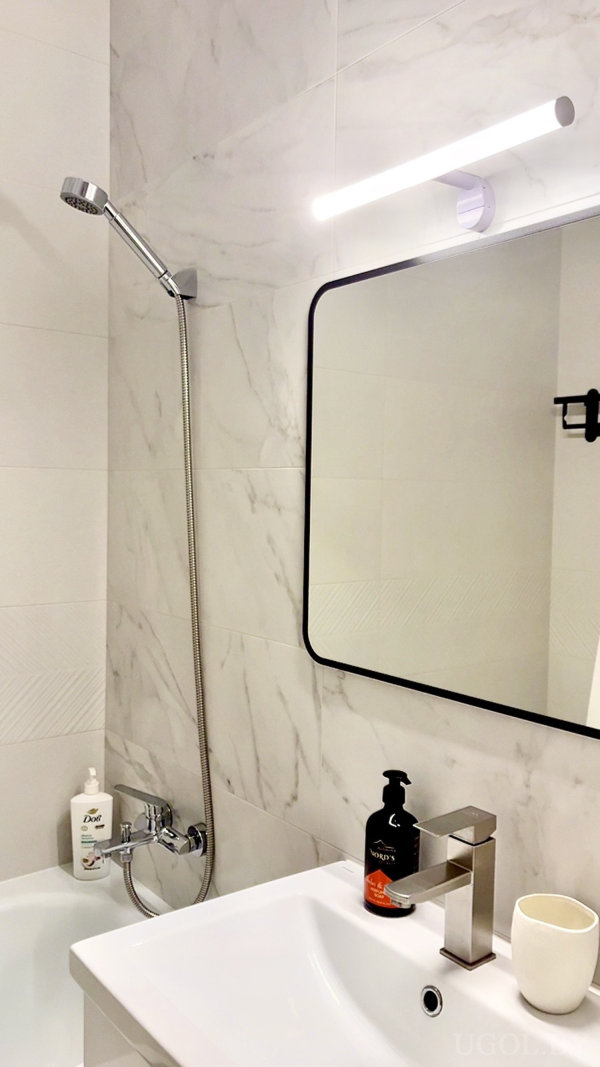 Интерьер с душем, умывальником, подсветкой, флаконом Dove и чёрной рамкой зеркала.