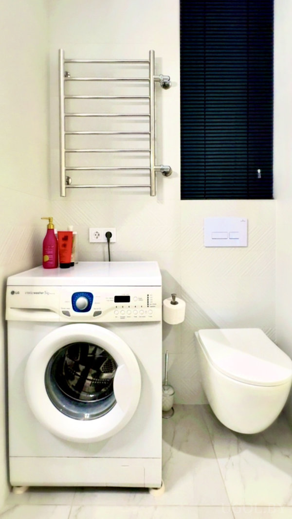 Компактная зона с унитазом, машиной, полотенцесушителем, аксессуарами и мраморным полом.