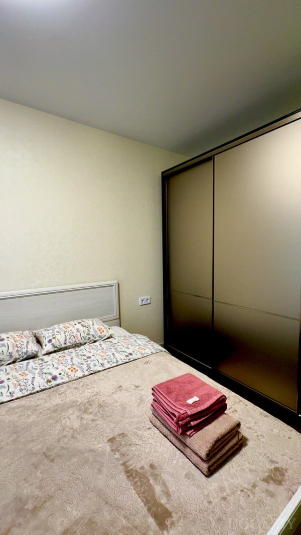 Комната с кроватью, сложенными полотенцами, цветочным постельным бельём, матовым шкафом-купе и бежевыми стенами.