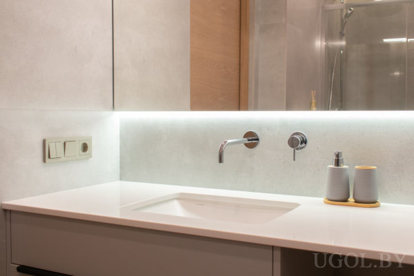 Современная зона умывальника с настенным смесителем, подсветкой под зеркалом, мыльницей и стеклянной перегородкой душевой.