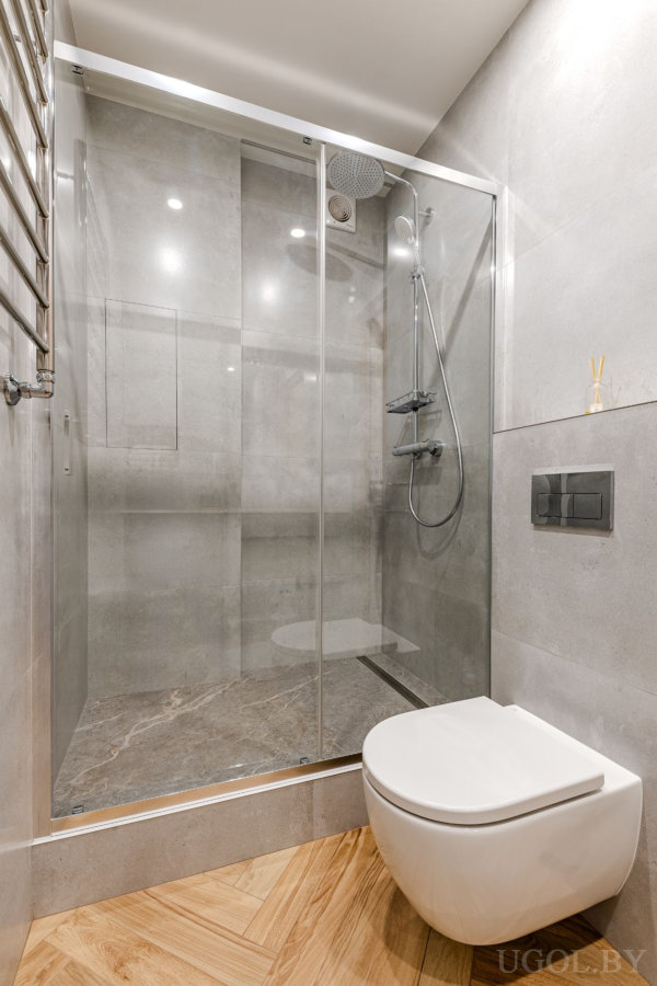 Современная ванная с душевой кабиной из стекла, подвесным унитазом, мраморной плиткой и деревянным полом ёлочкой.