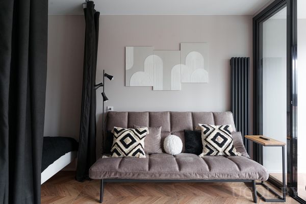 Современная гостиная с серым диваном, декоративными подушками, настенным светильником и деревянным столиком рядом.