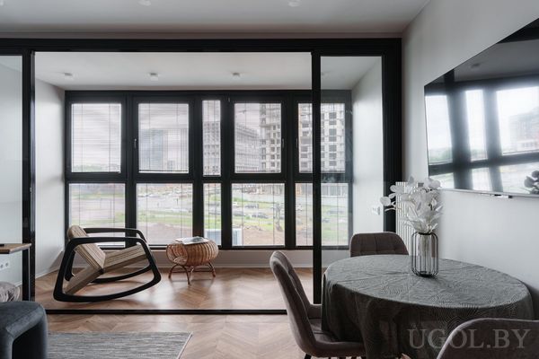 Стильные апартаменты с круглым столом и креслами, вазой с цветами, креслом‑качалкой и панорамным видом на город.