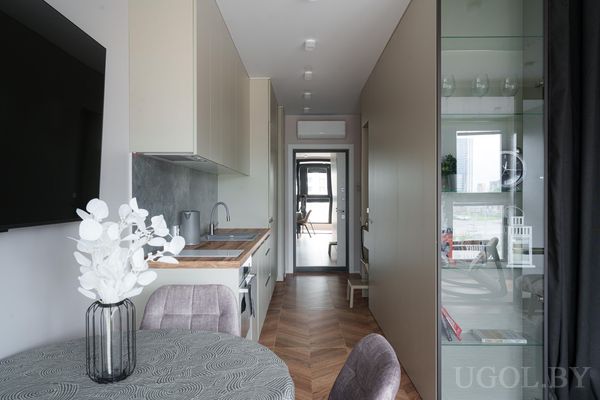 Узкая кухня с деревянной столешницей, круглым столом с цветами и телевизором на стене.