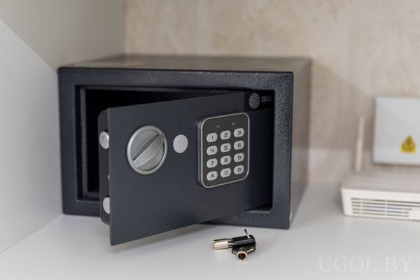 Чёрный электронный сейф с открытой дверцей, кодовой панелью и ключом на поверхности рядом.